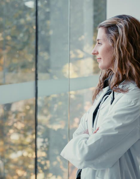 Eine Ärztin schaut gedankenverloren aus einem Fenster.